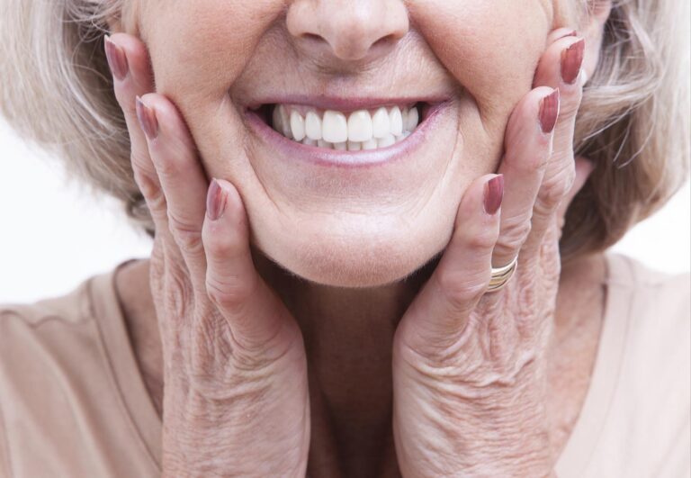Older woman smiling confidently, revealing well-fitted dentures that highlight dental health and restored function.